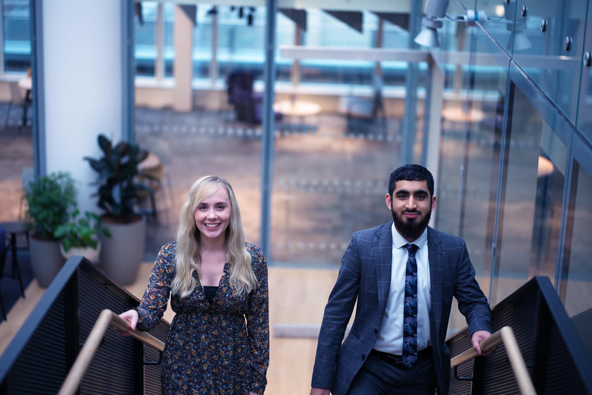 Two graduate colleagues going up stairs and smiling